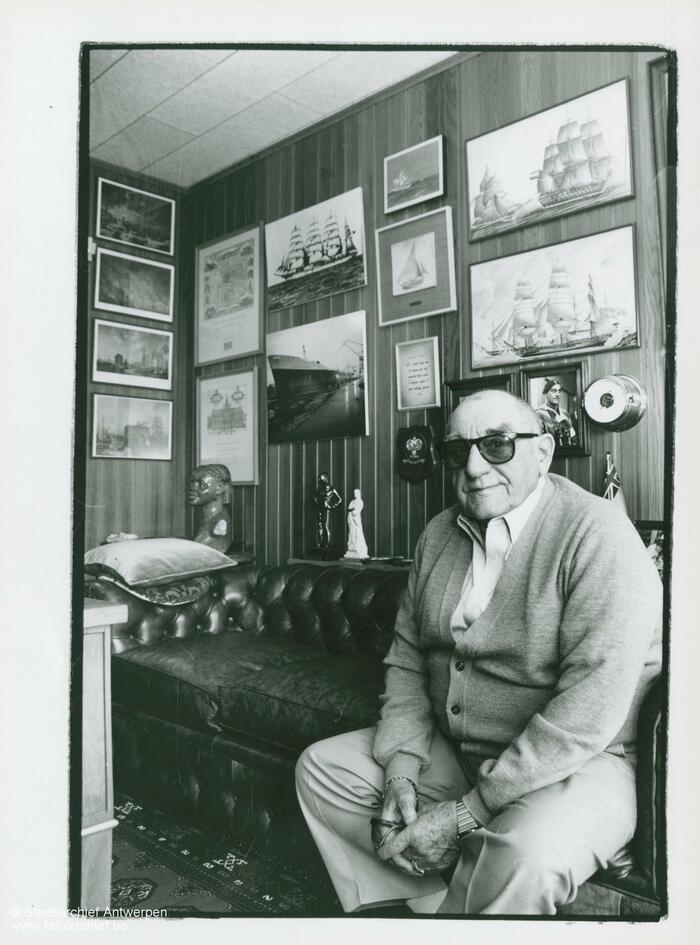 Eugène Colson auf einem Sofa vor einer Wand voller Bilder
